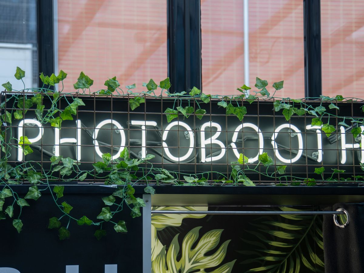 A lit photo booth sign framed by trailing greenery at a venue